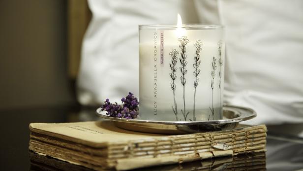 Eine brennende Duftkerze der Marke Lucy Annabella Organics steht auf einem alten Buch.