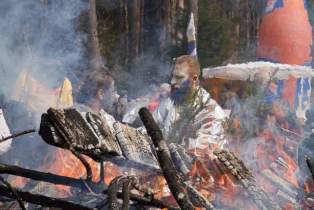 Zwei Männer mit bemalten Gesichtern sitzen an einem Lagerfeuer.