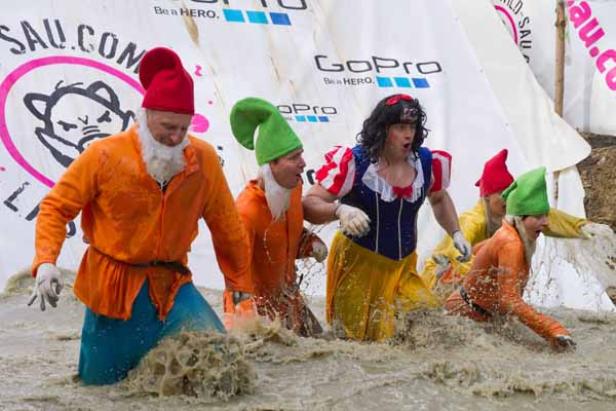Mehrere Personen in Kostümen, darunter Schneewittchen und Zwerge, waten durch schlammiges Wasser.