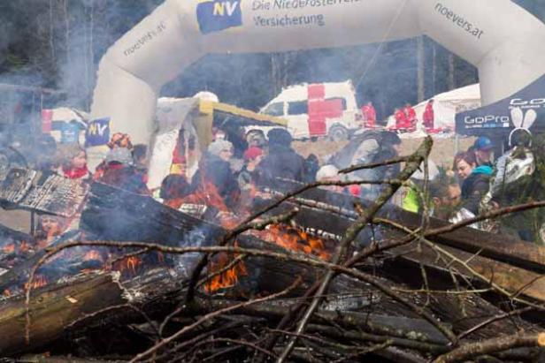 Ein großes Lagerfeuer brennt vor einer Menschenmenge und einem Sanitätswagen.