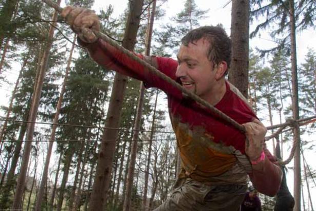 Ein Mann überquert eine Hindernisstrecke, an einem Seil hängend.