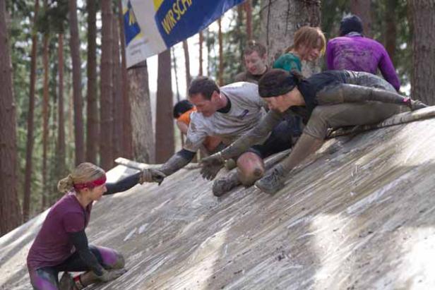 Teilnehmer helfen sich gegenseitig bei einem Hindernislauf über eine schräge Rampe.