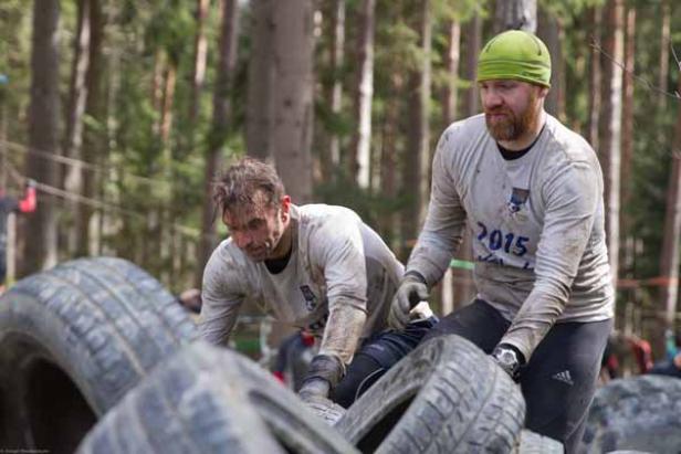 Zwei Männer überwinden ein Hindernis aus Reifen bei einem Hindernislauf.