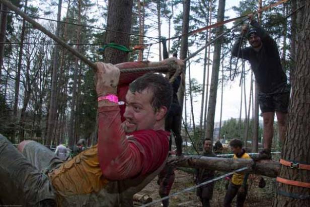 Ein Mann überquert eine Hindernisstrecke im Wald, während andere zusehen.