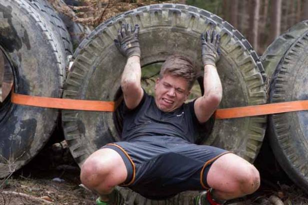 Ein Mann zwängt sich bei einem Hindernislauf durch einen Reifenparcours.