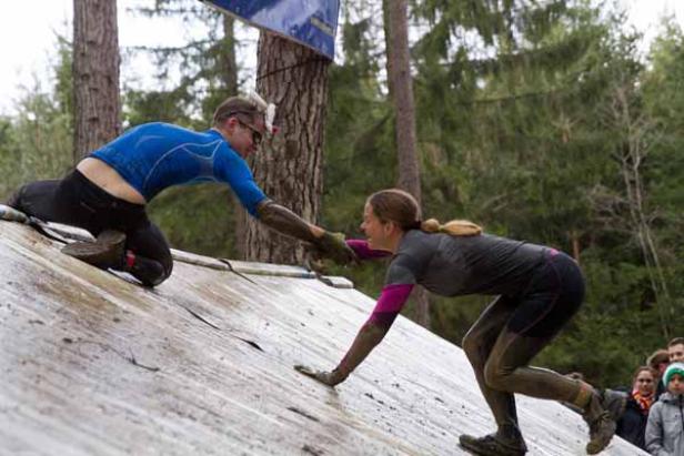 Ein Mann hilft einer Frau, eine schräge Wand bei einem Hindernislauf zu überwinden.