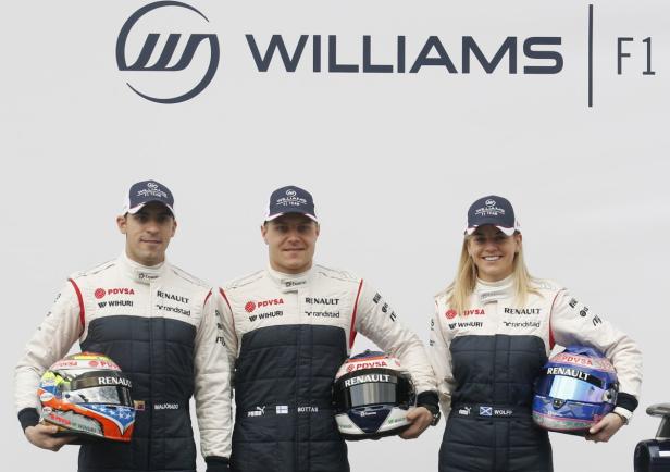 Drei Williams F1-Fahrer, darunter Susie Wolff, posieren mit ihren Helmen vor dem Williams-Logo.