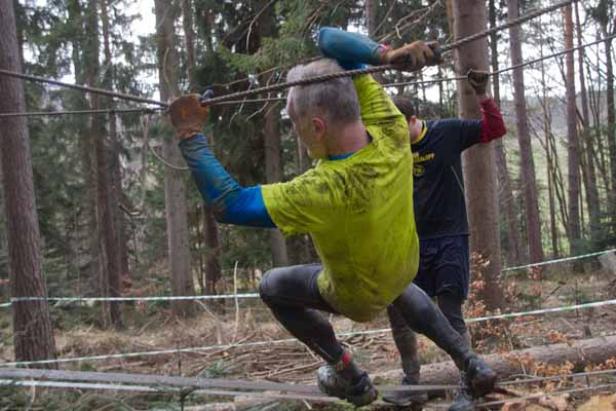 Ein Mann überquert eine Seilbrücke während eines Hindernislaufs im Wald.