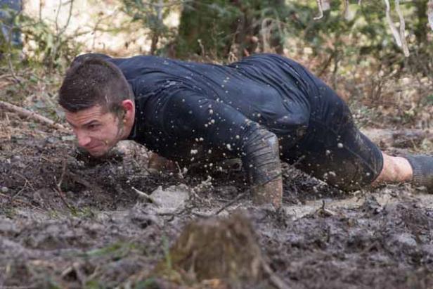 Ein Mann kriecht durch den Schlamm bei einem Hindernislauf.