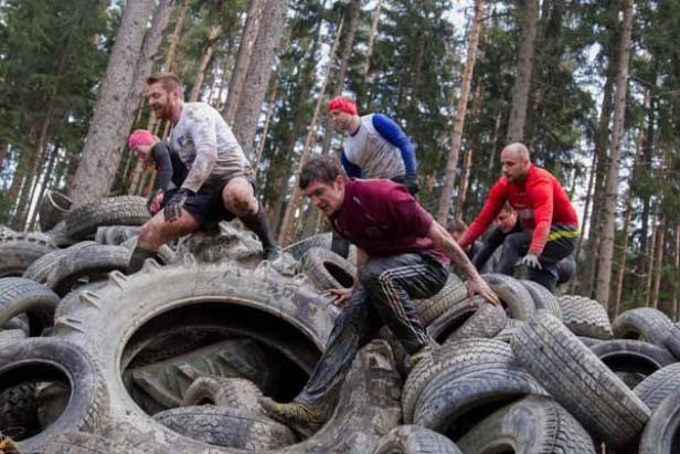 Mehrere Personen klettern über einen Haufen alter Reifen bei einem Hindernislauf.