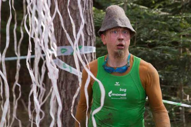 Ein Mann mit Schwimmbrille und grünem Shirt steht überrascht vor einer Baumabsperrung.