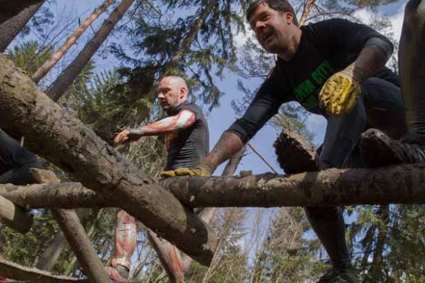 Zwei Männer klettern über eine Hindernisstrecke aus Baumstämmen.