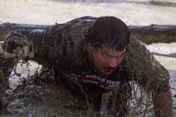 Ein Mann kriecht durch den Schlamm bei einem Hindernislauf.
