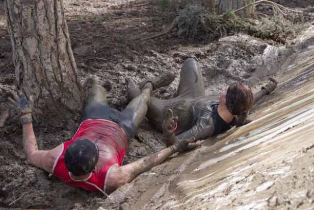 Zwei Personen liegen schlammbedeckt im Gelände.