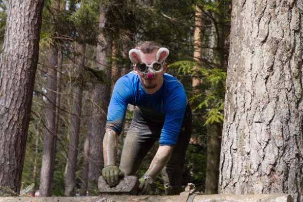 Ein Mann mit Hasenohren-Brille klettert über ein Hindernis im Wald.
