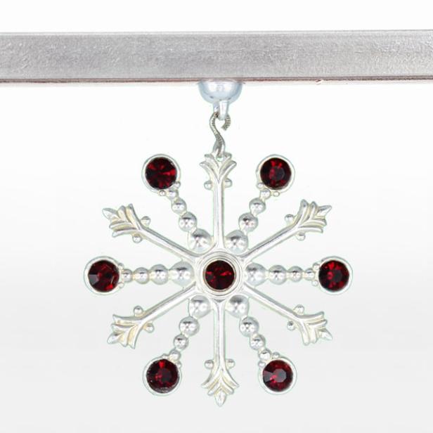 Ein silberner Schneeflocken-Anhänger mit roten Schmucksteinen hängt an einer Halterung.