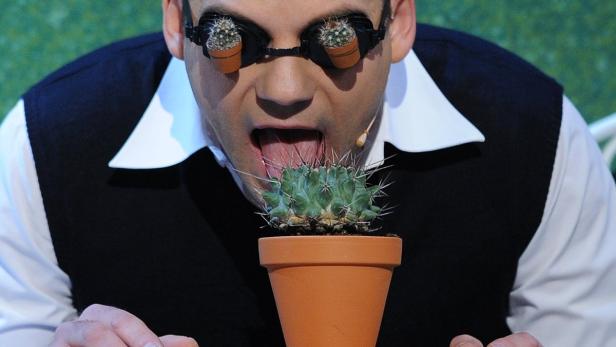 Ein Mann mit Kakteen auf den Augen führt einen Kaktus zum Mund.