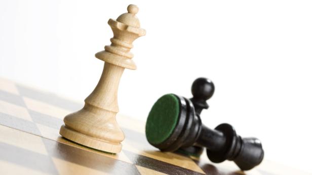 Eine weiße Dame steht neben einem gefallenen schwarzen Bauern auf einem Schachbrett.