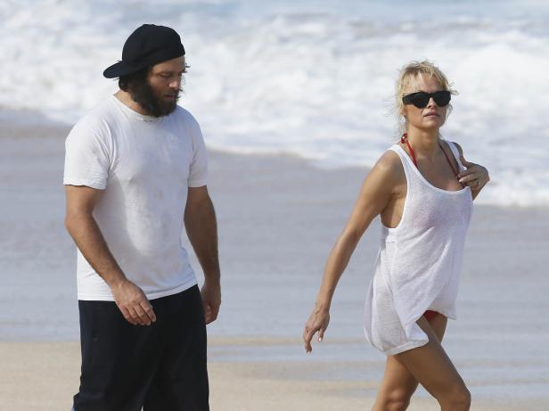 Pamela Anderson und ein Mann spazieren am Strand entlang.