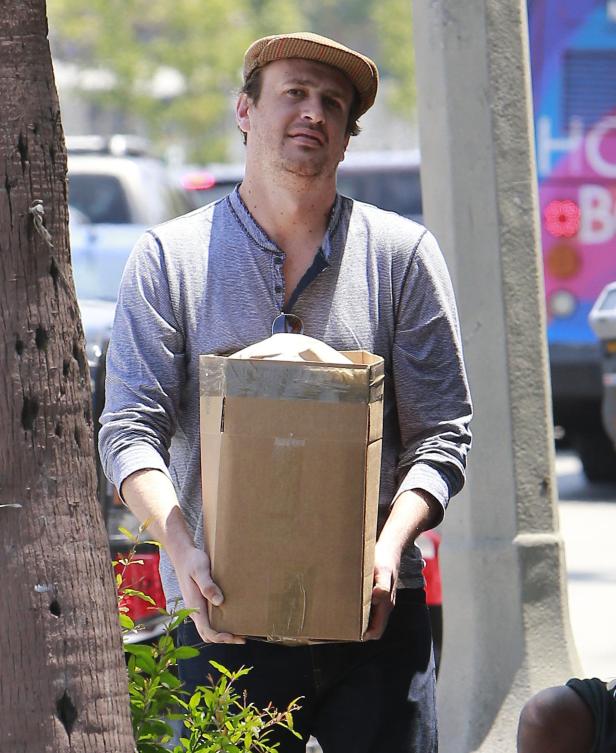 Jason Segel trägt eine braune Kappe und hält einen Karton.