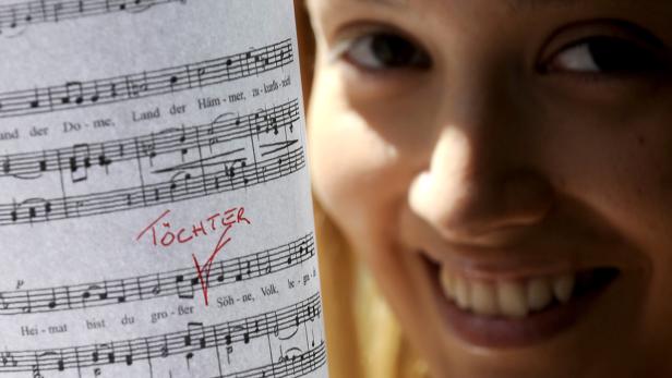 Eine Frau lächelt neben einem Notenblatt, auf dem das Wort „Töchter“ steht.
