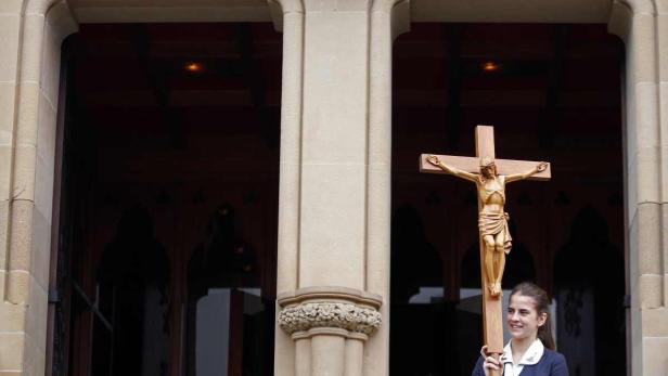 Ein junges Mädchen hält ein Holzkreuz vor dem Eingang einer Kirche.