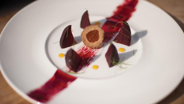 Ein Teller mit einem Fleischbällchen, roter Bete und gelben Saucenpunkten.