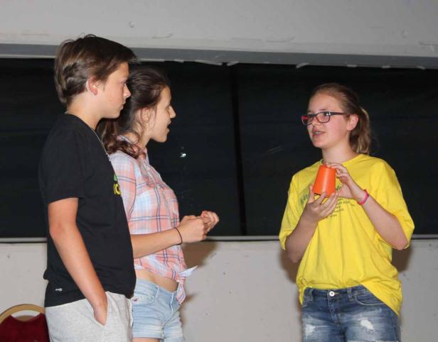 Drei Jugendliche stehen zusammen, ein Mädchen hält einen orangefarbenen Becher in den Händen.