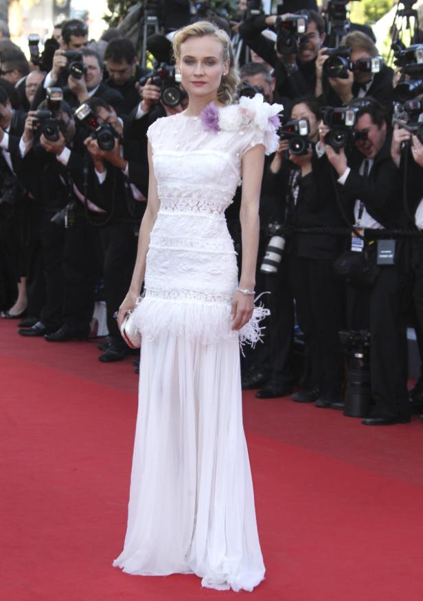 Diane Kruger in einem weißen Kleid auf dem roten Teppich, umringt von Fotografen.
