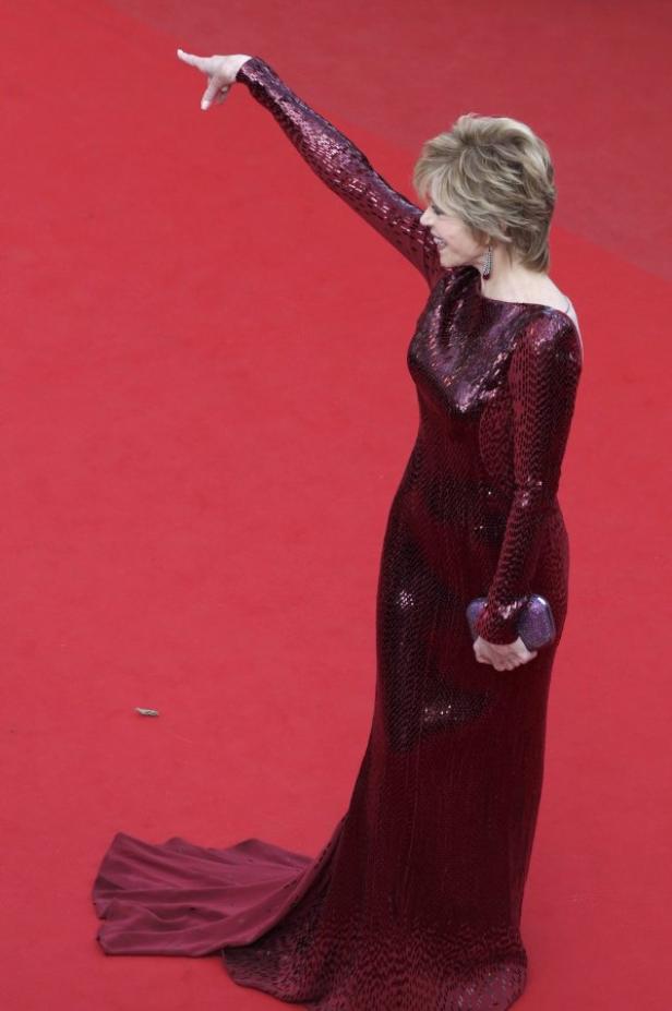 Jane Fonda in einem glitzernden, burgunderfarbenen Kleid auf einem roten Teppich.