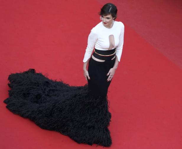 Eine Frau in einem eleganten, schwarz-weißen Kleid mit Federn auf einem roten Teppich.