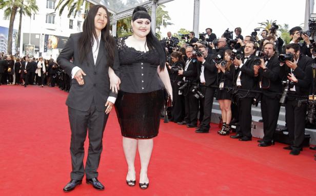 Beth Ditto und ein Begleiter posieren auf einem roten Teppich vor einer Wand von Fotografen.