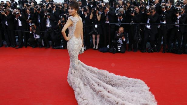Eva Longoria posiert in einem langen, hellen Kleid mit Schleppe auf dem roten Teppich, umringt von Fotografen.