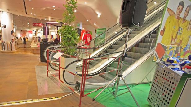 In einem Kaufhaus steht eine Rolltreppe neben einer DJ-Station und Dekorationen für ein Fußballereignis.