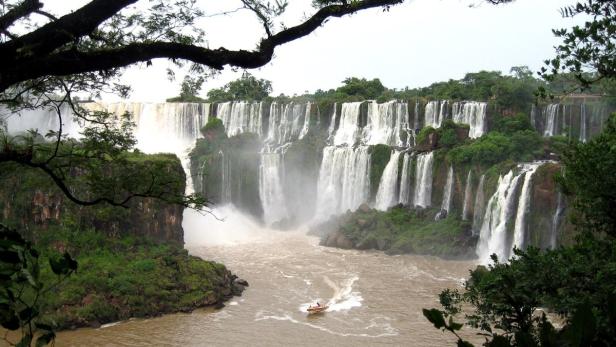 Die Iguazú-Wasserfälle stürzen in einen Fluss, auf dem ein kleines Boot fährt.