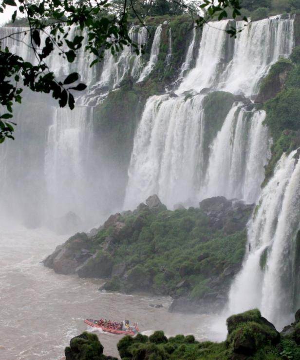 Ein Schnellboot mit Touristen fährt vor den tosenden Iguazú-Wasserfällen.
