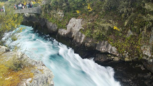 Tosendes, türkisfarbenes Wasser fließt durch eine enge Schlucht unter einer Brücke hindurch.