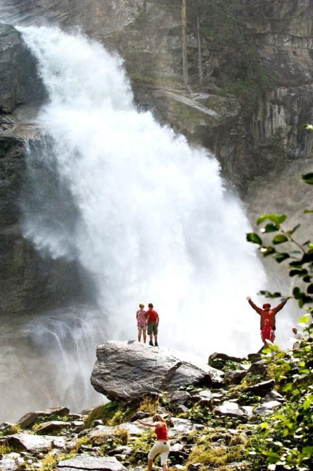 Mehrere Personen bewundern einen hohen Wasserfall in einer felsigen Landschaft.