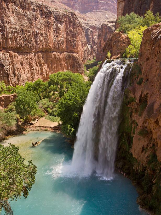 Ein Wasserfall ergießt sich in einen türkisfarbenen Pool, umgeben von roten Felswänden.