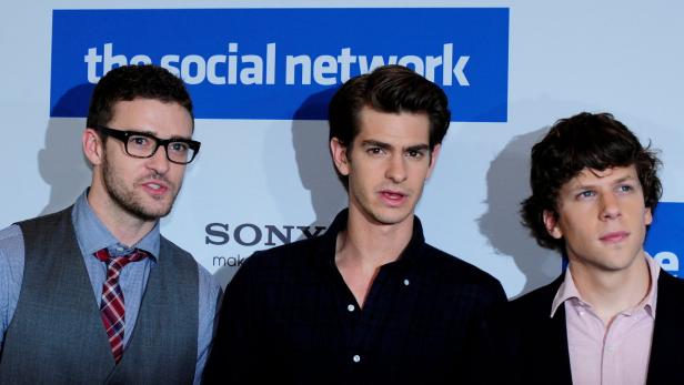 Justin Timberlake, Andrew Garfield und Jesse Eisenberg posieren vor einem „The Social Network“-Poster.