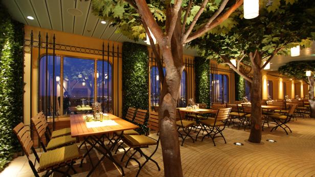 Ein Restaurant mit Tischen und Stühlen, umgeben von Bäumen und Pflanzen.