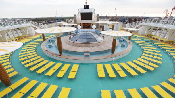 Blick auf das Sonnendeck eines Kreuzfahrtschiffes mit gelben Liegestühlen und Sonnenschirmen.