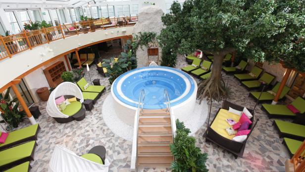 Ein Whirlpoolbereich mit Liegen und einem Baum auf einem Kreuzfahrtschiff.