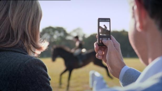 Eine Person fotografiert mit einem Handy eine Reiterin auf einem Pferd.