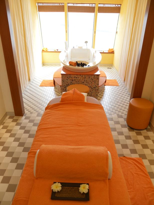 Ein Spa-Raum mit einer Massageliege und einer Badewanne vor einem hellen Fenster.