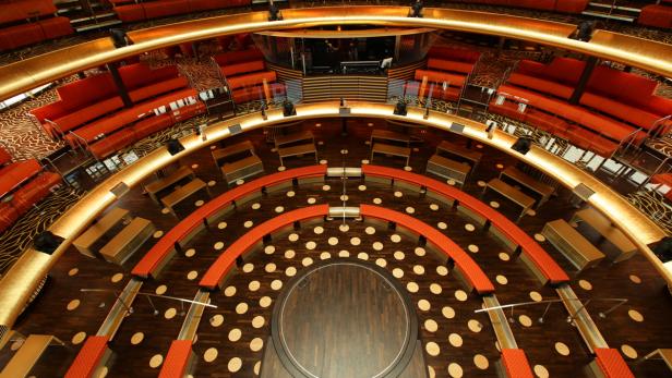 Blick von oben auf eine Bühne mit kreisförmigen Sitzreihen und roter Polsterung.