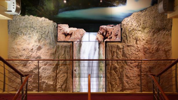 Eine künstliche Felswand mit einem Wasserfall-Display in der Mitte, gesehen von einem Treppenabsatz.