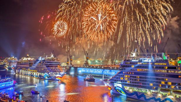 Mehrere AIDA-Kreuzfahrtschiffe liegen im Hafen, während ein Feuerwerk den Nachthimmel erhellt.