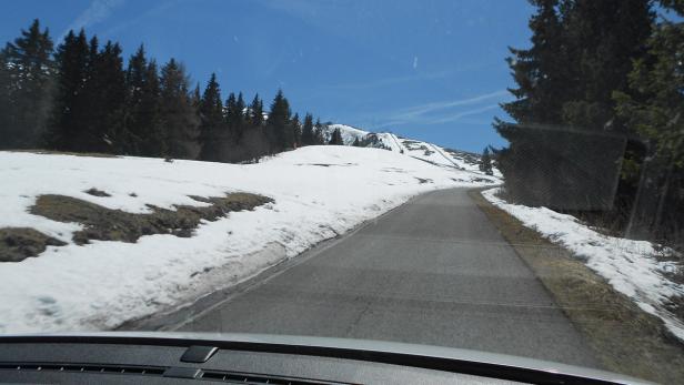 Eine Straße führt durch eine teilweise schneebedeckte Berglandschaft.
