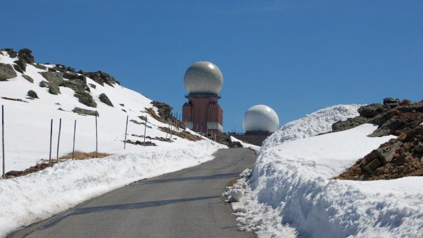 Eine Straße führt zu zwei Radarstationen auf einem schneebedeckten Berg.